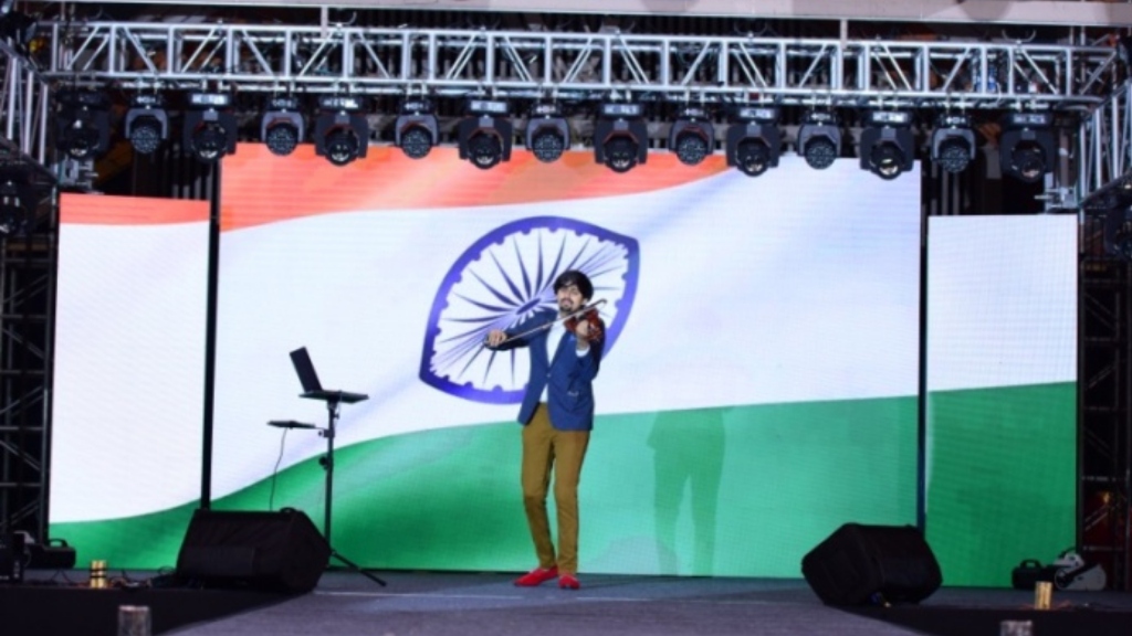 Violinist playing on stage in front of Indian flag screen